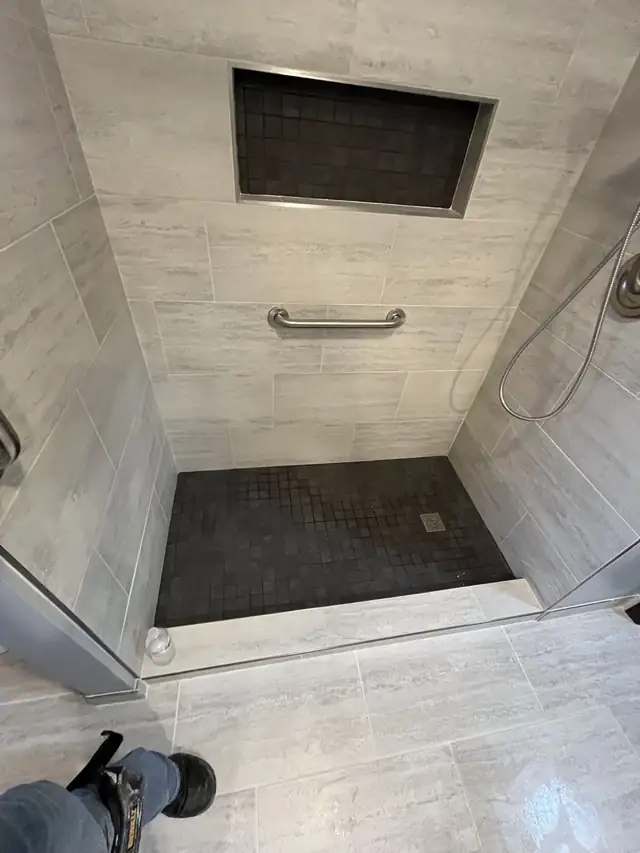 Tiled walk-in shower with wood-look wall tile, dark mosaic floor and a grab bar