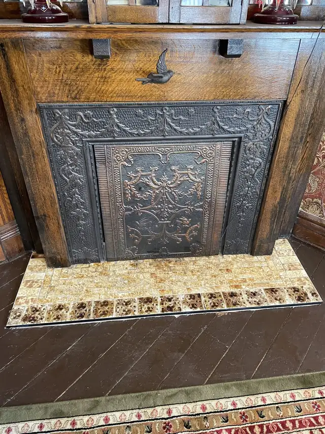 Fireplace hearth restored with antique salvaged tiles in front of an ornate cast iron fireplace cover