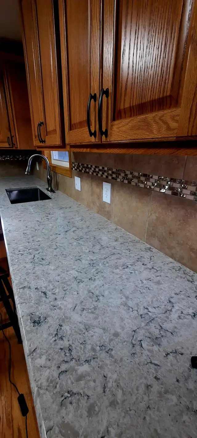 Kitchen backsplash of large brown tile with a glass and stone mosaic accent band above a light quartz countertop