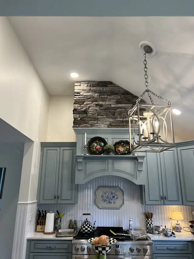 Stacked stone accent above a sage green range hood in a kitchen with a lantern pendant
