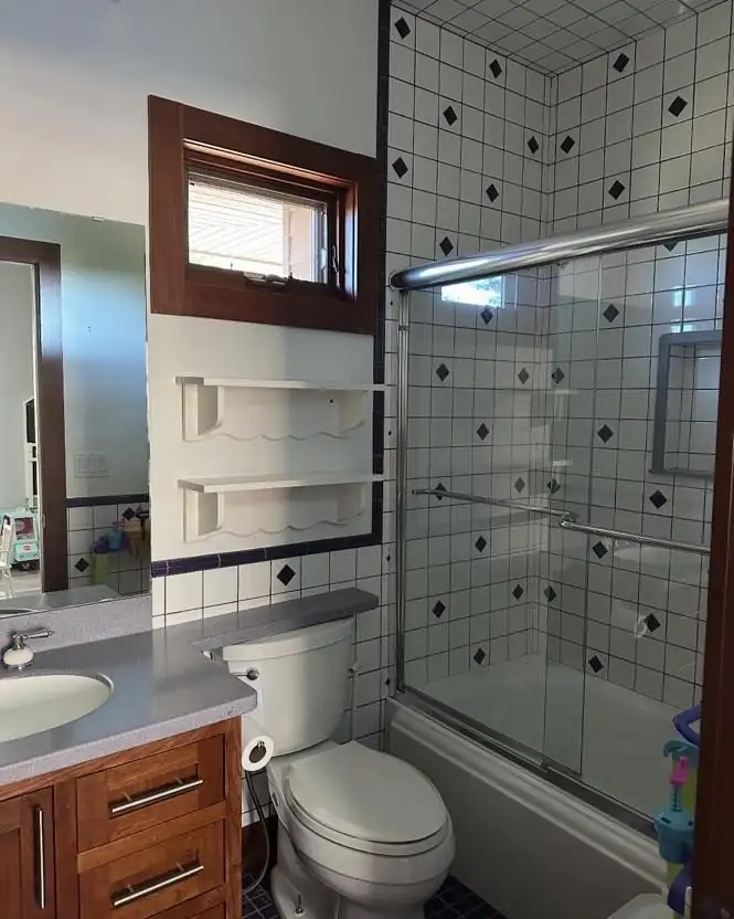 Tub and shower with white tile, black diamond accents, built-in shelves and glass doors