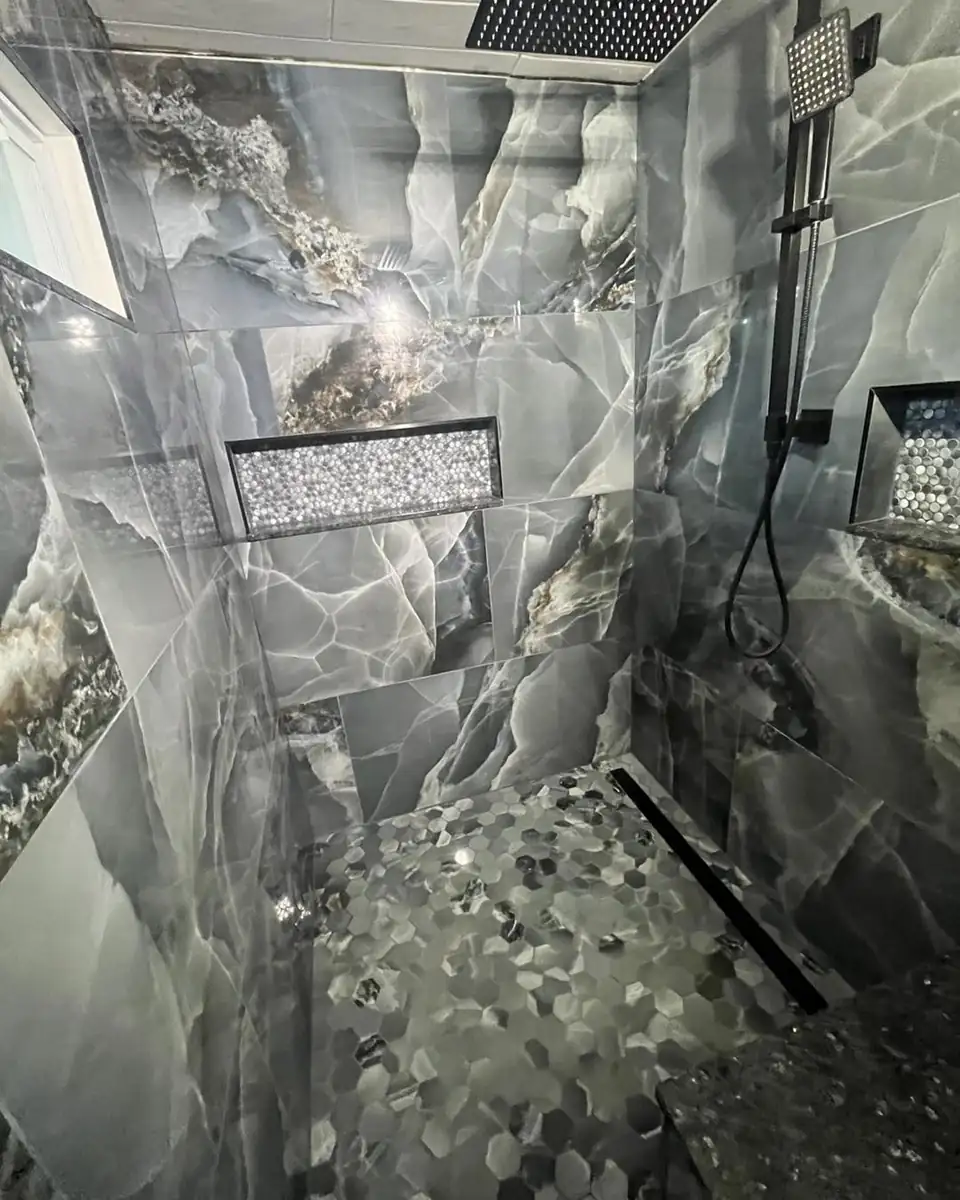 Custom tile showers in Bay City, MI by Janke Custom Tile: large gray marble-look porcelain walls, pebble mosaic niche and floor, linear drain and glass panel
