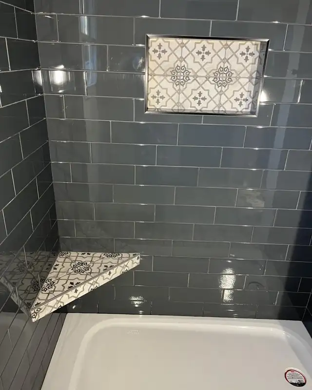 Shower in dark gray glass subway tile with a patterned tile bench top and window